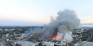 A large industrial fire with thick smoke rising into the sky and firefighters responding