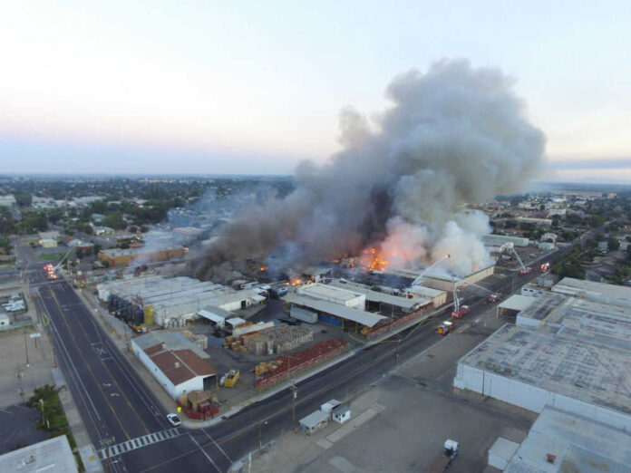1062550499 A large industrial fire with thick smoke rising into the sky and firefighters responding