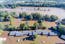 Flooded landscape with submerged buildings and vehicles.