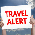 Hands holding travel alert sign against sky