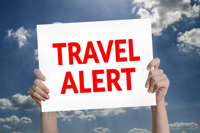 429811915 Hands holding travel alert sign against sky