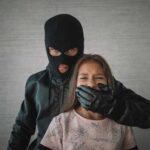A masked figure holding a girl, covering her mouth