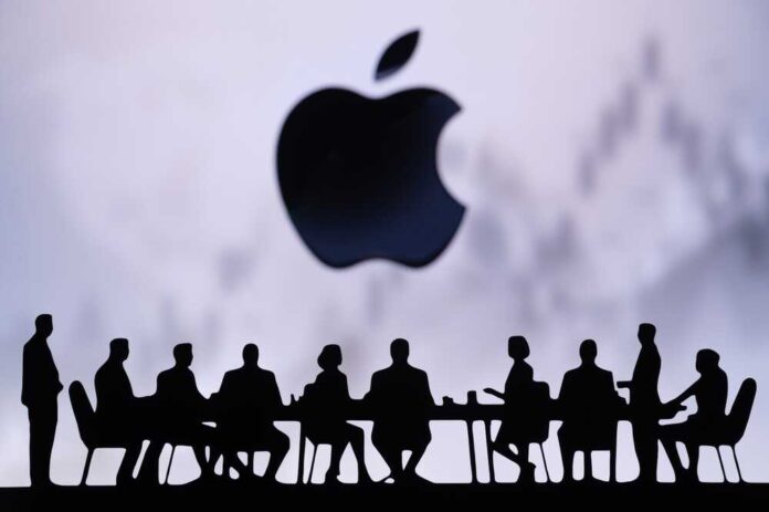 shutterstock_2528432367.jpg Silhouettes of people in a meeting with an Apple logo in the background
