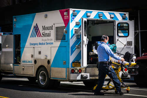 A healthcare worker pushing a stretcher next to an ambulance