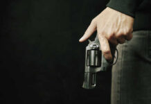 Close-up of a hand holding a revolver against a dark background