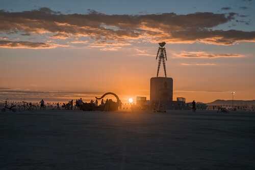 Silhouettes of people and an art installation against a sunset backdrop