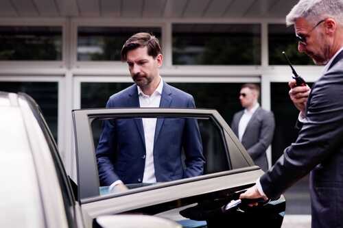 A man in a suit approaching a luxury car with a security guard nearby