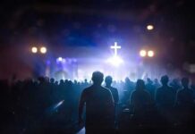 Silhouetted figures in a crowd during a worship service with a cross in the background