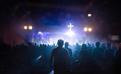 Silhouetted figures in a crowd during a worship service with a cross in the background