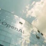 Exterior view of the OpenAI building with a reflective glass facade under a cloudy sky