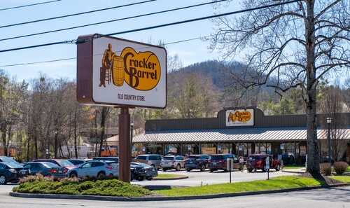Exterior view of a Cracker Barrel restaurant with a parking lot and mountains in the background