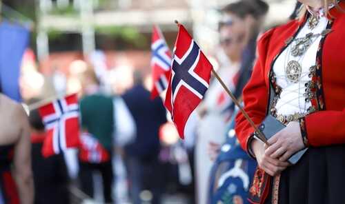 Person in traditional Norwegian attire holding a small flag during a celebration