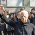 A man with white hair waving to a crowd