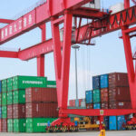 A large red crane at a shipping port lifting cargo containers