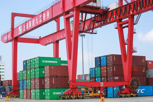 shutterstock_2007467771.jpg A large red crane at a shipping port lifting cargo containers