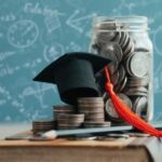 Graduation cap on a stack of coins next to a jar of coins and a pencil
