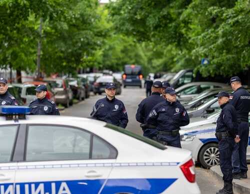 Group of police officers gathered on a street near parked cars