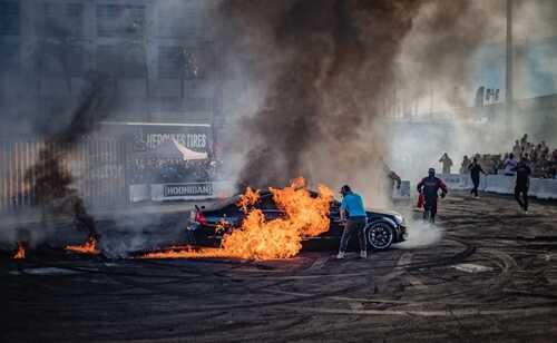 shutterstock_2388049705.jpg A car engulfed in flames at a motorsport event with spectators in the background