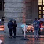 People gathered under umbrellas at a memorial site with candles