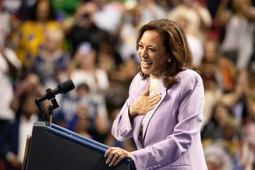 shutterstock_2501957419.jpg A female politician smiling while speaking at a podium in front of an engaged audience
