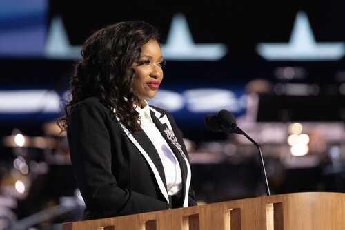 A woman in formal attire speaking at a podium on stage
