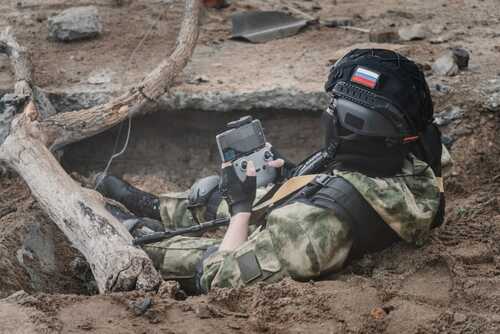 Soldier in tactical gear using a device while lying in a trench
