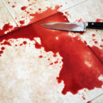 A bloody knife lying next to a pool of blood on tiled flooring