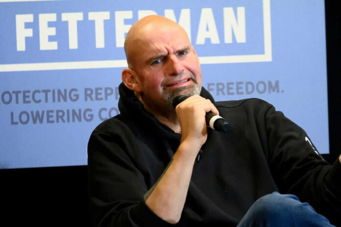 Man holding microphone, sitting under Fetterman sign.