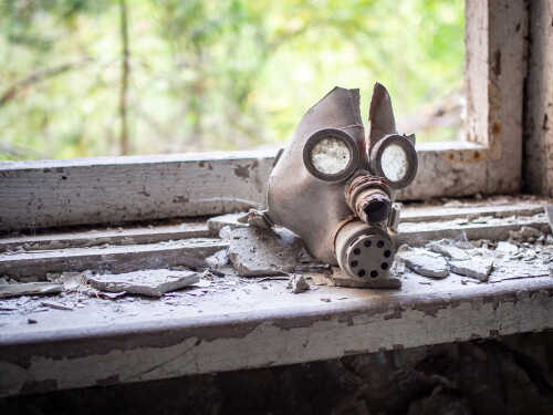 shutterstock_1495627391.jpg A worn gas mask resting on a dusty windowsill in an abandoned building