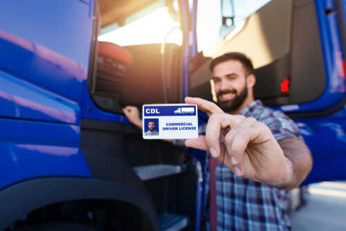 Man holding a commercial driver's license in front of a blue truck