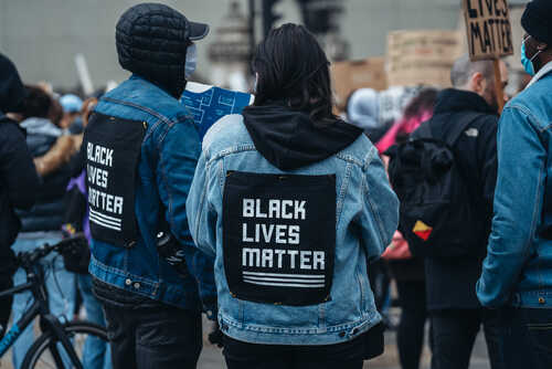 Two individuals wearing denim jackets with 'Black Lives Matter' patches at a protest