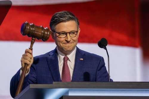 A speaker holding a gavel at a political event with an American flag backdrop