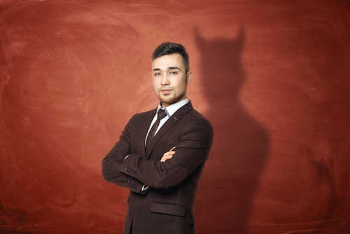A man in a suit standing confidently with a shadow resembling devil horns on a red background
