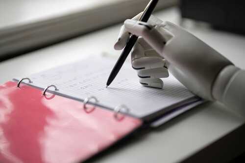A robotic hand holding a pen, writing in a notebook