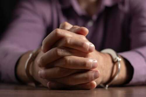 Close-up of clasped hands with handcuffs on a wooden table