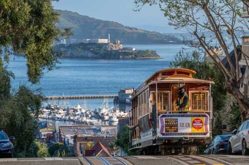 A cable car traveling down a hill with a harbor view in the background