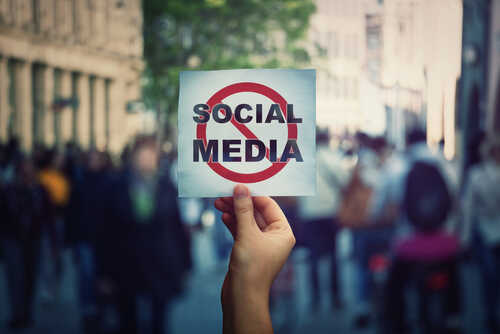 shutterstock_1743875402.jpg A hand holding a sign that says 'SOCIAL MEDIA' with a prohibition symbol