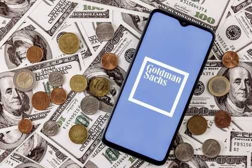 Smartphone displaying Goldman Sachs logo surrounded by various coins and dollar bills