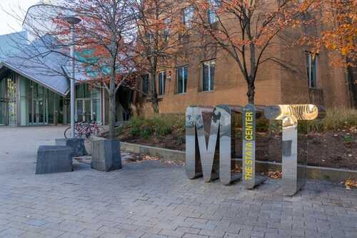 Signage displaying 'MIT' in front of the Stata Center on a campus with autumn trees