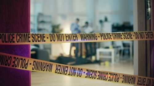 Police crime scene tape blocking an area with investigators in the background