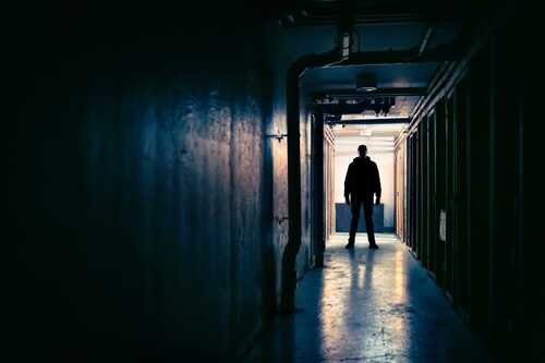 Silhouette of a person standing in a dark hallway with light at the end