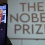 A smartphone displaying a portrait of a political figure with a projection of 'The Nobel Prize' in the background