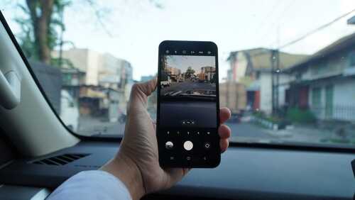 Person holding a smartphone capturing a street view from a car