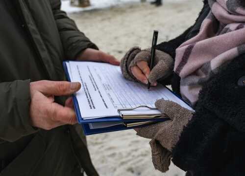 Person signing a document outdoors while another holds the clipboard