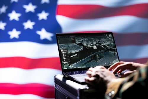 Person using a laptop with a surveillance interface in front of an American flag