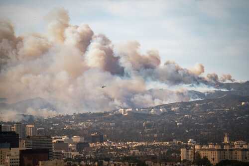 shutterstock_2568781365.jpg A wildfire producing thick smoke over a city landscape with a helicopter in the sky