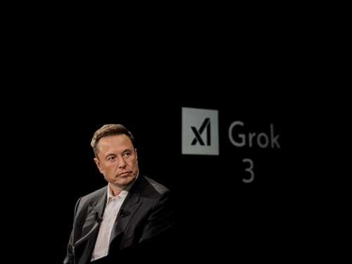 Elon Musk speaking at a technology event with a presentation backdrop