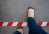 A person's foot stepping over a red and white striped warning line on the ground