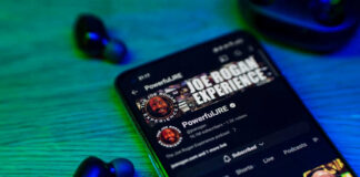 Smartphone displaying podcast with wireless earbuds nearby.