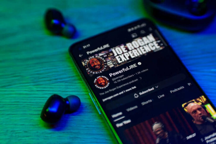 Smartphone displaying podcast with wireless earbuds nearby.